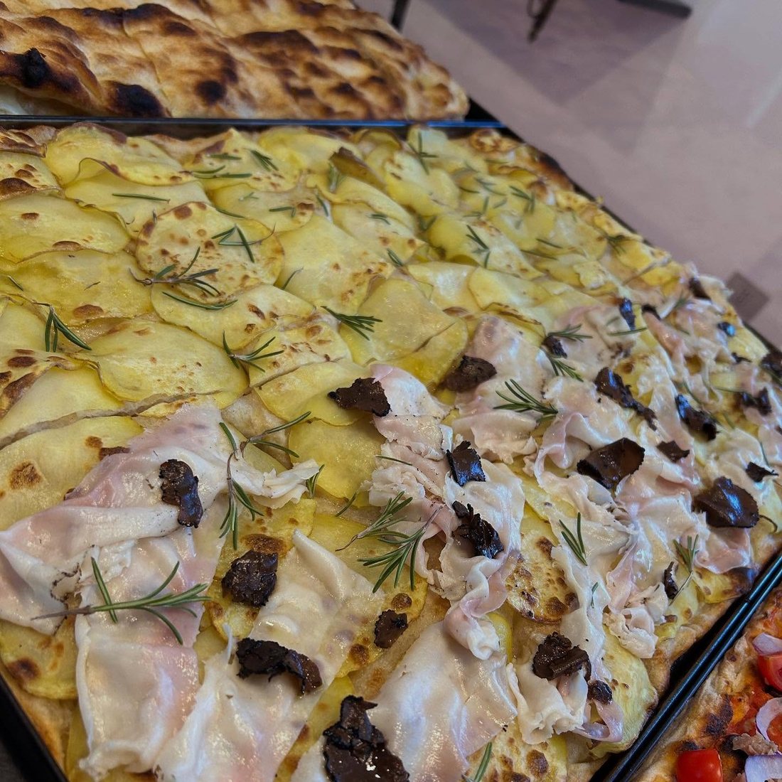 Teglie di pizza con patate e rosmarino e con prosciutto cotto e tartufo esposte al banco